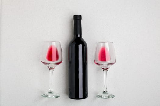 Overhead angled view of a large bottle of red wine, drinking glasses on white background. Top view. Copy space