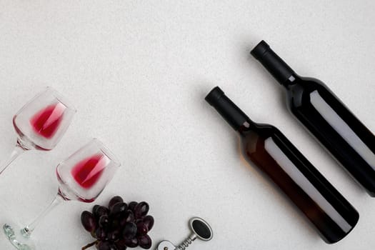 Two glasses of red wine and grapes. Two bottles of wine and a corkscrew. Top view with copy space