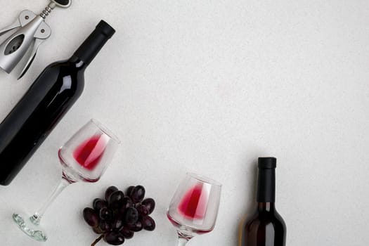 Two glasses of red wine and grapes. Two bottles of wine and a corkscrew. Top view with copy space