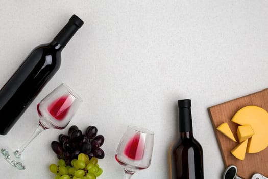 Two glasses of red wine, cheese and grapes. Two bottles of wine and a corkscrew. Top view with copy space