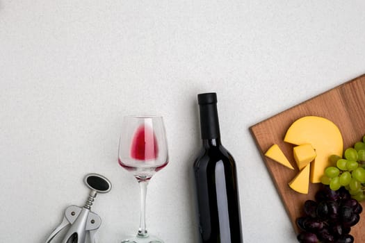 Glass of red wine, cheese and grapes. Bottle of wine and a corkscrew. Top view with copy space