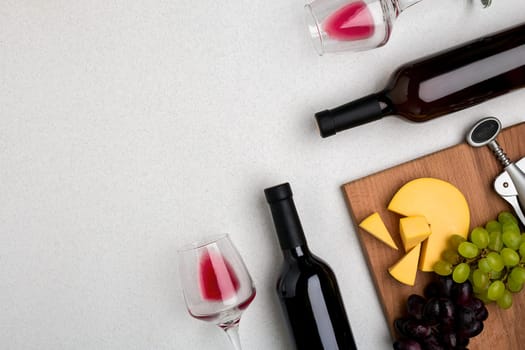 Two glasses of red wine, cheese and grapes. Two bottles of wine and a corkscrew. Top view with copy space