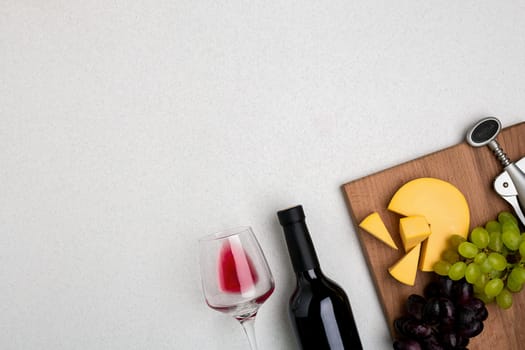 Glass of red wine, cheese and grapes. Bottle of wine and a corkscrew. Top view with copy space