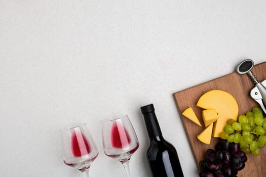 Two glasses of red wine, cheese and grapes. Bottle of wine and a corkscrew. Top view with copy space