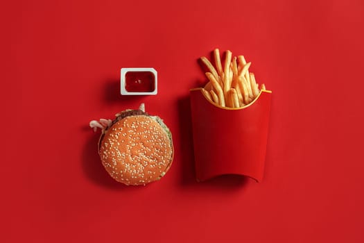 Burger and Chips. Hamburger and french fries in red paper box. Fast food on red background. Hamburger with tomato sauce. Top view, flat lay with copyspace