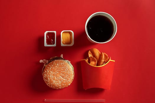 Concept of mock up burger, potatoes, sauce and drink on red background. Copy space for text and logo. Flat lay
