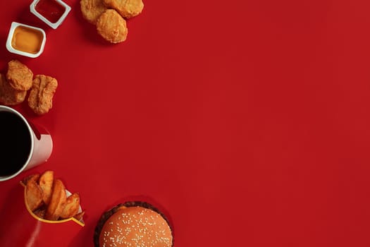 Concept of mock up burger, potatoes, sauce, chicken nuggets and drink on red background. Copy space for text and logo. Flat lay
