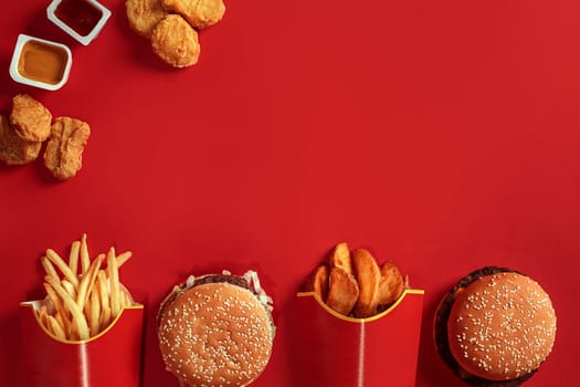 Burger and Chips. Hamburger and french fries in red paper box. Fast food on red background. Hamburger with tomato sauce. Top view, flat lay with copyspace