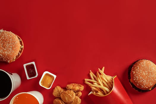 Two hamburgers and french fries, sauces and drinks on red background. Fast food. Hamburger with chicken nuggets. Top view, flat lay with copyspace.