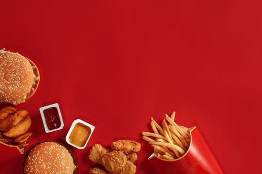 Burger and Chips. Hamburger and french fries in red paper box. Fast food on red background. Hamburger with tomato sauce. Top view, flat lay with copyspace