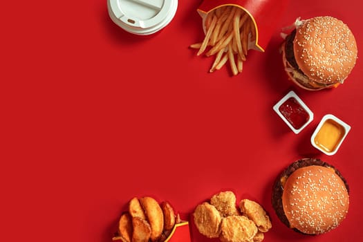 Fast food dish top view. Meat burger, potato chips and glass of drink on red background. Takeaway composition. Wrapped French fries, hamburger, mayonnaise and ketchup sauces on red desk. Copy space