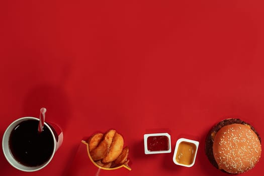 Concept of mock up burger, potatoes, sauce and drink on red background. Copy space for text and logo. Flat lay