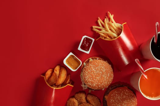 Two hamburgers and french fries, sauces and drinks on red background. Fast food. Hamburger with chicken nuggets. Top view, flat lay with copyspace.