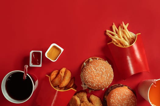 Two hamburgers and french fries, sauces and drinks on red background. Fast food. Hamburger with chicken nuggets. Top view, flat lay with copyspace.