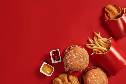 Two hamburgers and french fries, sauces on red background. Fast food. Top view, flat lay with copyspace.