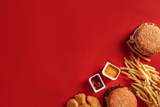Burger and Chips. Hamburger and french fries in red paper box. Fast food on red background. Hamburger with tomato sauce. Top view, flat lay with copyspace