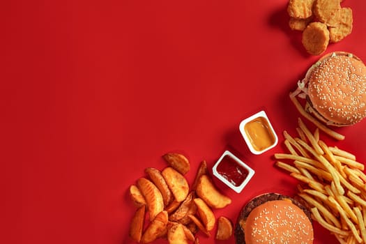 Burger and Chips. Hamburger and french fries in red paper box. Fast food on red background. Hamburger with tomato sauce. Top view, flat lay with copyspace