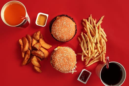 Burger and Chips. Hamburger and french fries in red paper box. Fast food on red background. Hamburger with tomato sauce. Top view, flat lay with copyspace