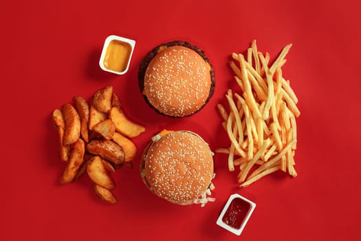 Burger and Chips. Hamburger and french fries in red paper box. Fast food on red background. Hamburger with tomato sauce. Top view, flat lay with copyspace