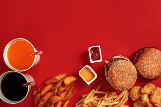 Burger and Chips. Hamburger and french fries in red paper box. Fast food on red background. Hamburger with tomato sauce. Top view, flat lay with copyspace