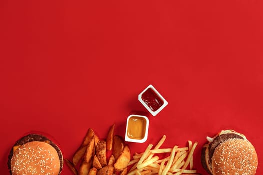 Fast food dish top view. Meat burger, potato chips and nuggets on red background. Takeaway composition. Wrapped French fries, hamburger, mayonnaise and ketchup sauces on red desk. Top view. Copy space