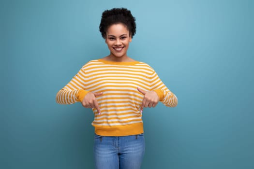 positive brunette latin young woman with ponytail in yellow sweater on studio background.