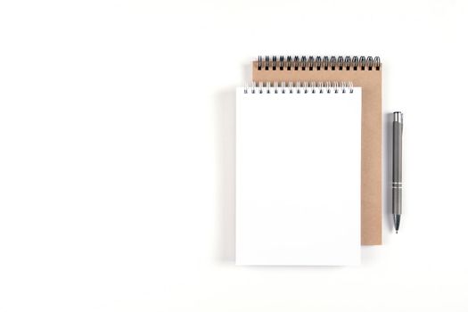 Two blank spiral notepads stacked on a white background next to an automatic pen. Notebooks with white and recycled sheets. Education, office.