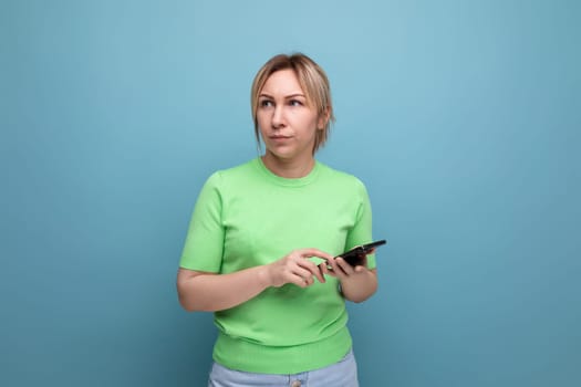 indignant attractive blond girl with gadgets in her hand on a blue background with copy space.