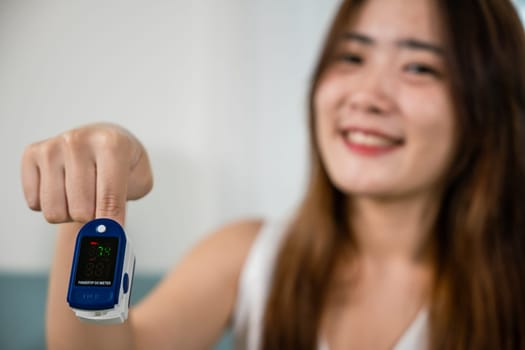 Young woman finger inserted into the pressure oximeter to assess health under sofa in living room at home, Self healthcare with corona virus pandemic, medical health care concept