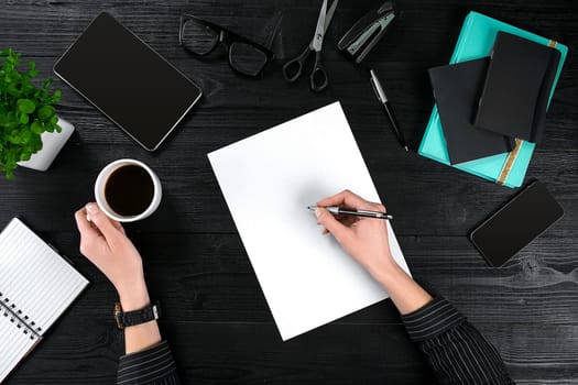 Businesswoman desk with with different objects. A woman's hand writes in a notebook. Top view. Flat lay