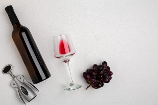 Overhead angled view of a large bottle of red wine, drinking glass on white background. Top view. Copy space