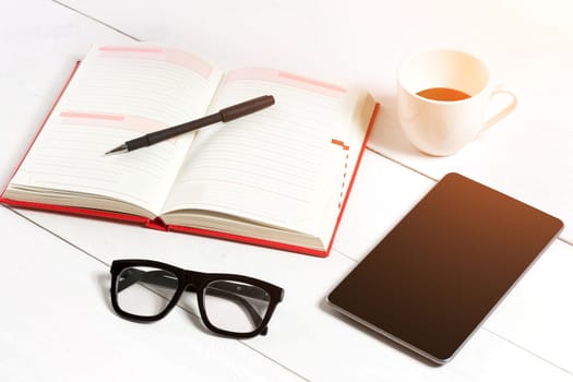 Office table desk with set of supplies, white blank notepad, cup, pen, tablet, glasses, flower on white background. Top view and copy space for text