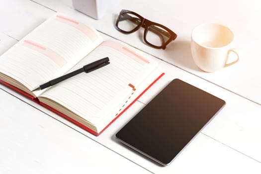 Stylish minimalistic workplace with tablet and notebook and glasses in flat lay style. White background. Top view. Copy space. sun flare