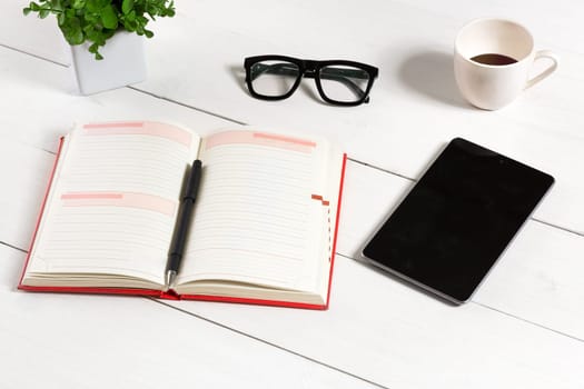 Office table desk with set of supplies, white blank notepad, cup, pen, tablet, glasses, flower on white background. Top view and copy space for text