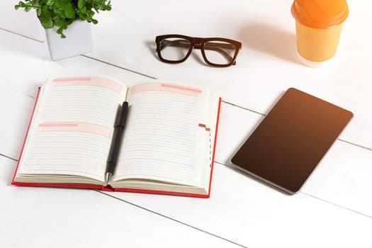 Stylish minimalistic workplace with tablet and notebook and glasses in flat lay style. White background. Top view. Copy space. sun flare