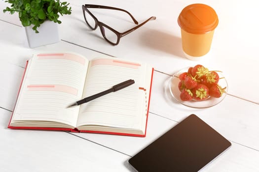 Office table desk with set of supplies, white blank notepad, cup, pen, tablet, glasses, flower on white background. Top view and copy space for text