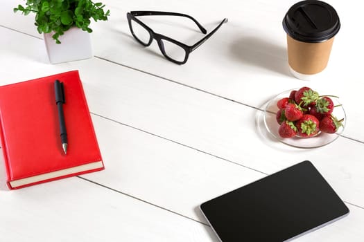 Office table desk with set of supplies, red notepad, cup, pen, tablet, glasses, flower on white background. Top view and copy space for text