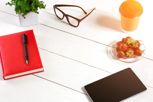 Office table desk with set of supplies, red notepad, cup, pen, tablet, glasses, flower on white background. Top view and copy space for text. sun flare