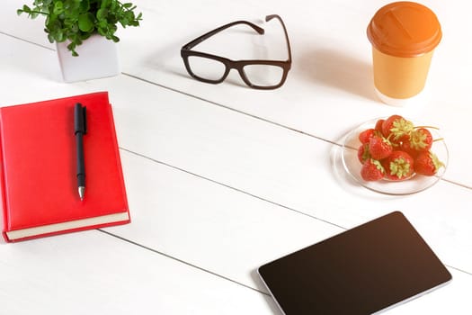 Office table desk with set of supplies, red notepad, cup, pen, tablet, glasses, flower on white background. Top view and copy space for text. sun flare