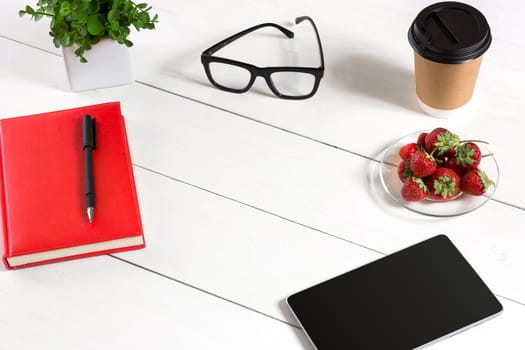 Office table desk with set of supplies, red notepad, cup, pen, tablet, glasses, flower on white background. Top view and copy space for text