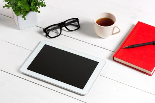 Office table desk with set of supplies, red notepad, cup, pen, tablet, glasses, flower on white background. Top view and copy space for text