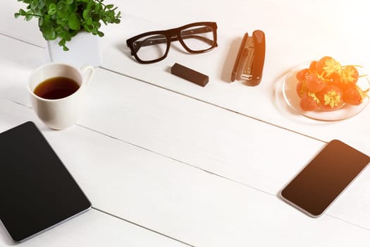 Modern workplace with digital tablet computer and mobile phone, cup of coffee and flower on white background. Top view and copy space for text. sun flare