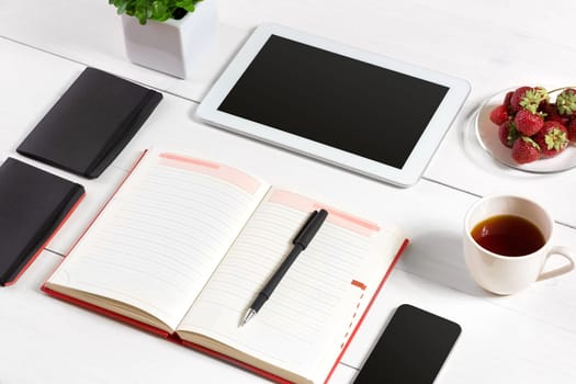 Office table desk with set of supplies, white blank notepad, cup, pen, tablet, glasses, flower on white background. Top view and copy space for text