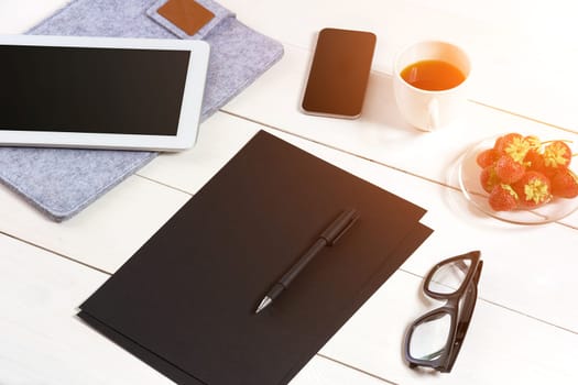 Modern workplace with digital tablet computer and mobile phone, cup of coffee, pen and empty sheet of paper. Top view and copy space for text. sun flare