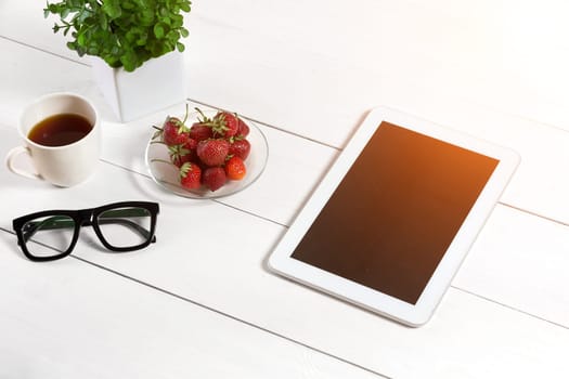 Flower pot, glasses, tablet on white desktop. White background. Top view. Copy space. Sun flare