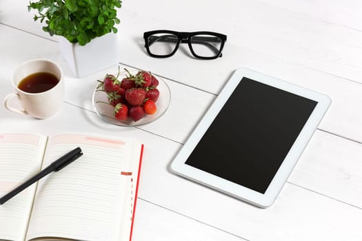 Office table desk with set of supplies, white blank notepad, cup, pen, tablet, glasses, flower on white background. Top view and copy space for text