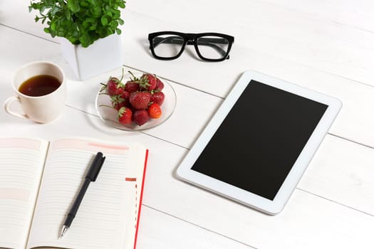 Office table desk with set of supplies, white blank notepad, cup, pen, tablet, glasses, flower on white background. Top view and copy space for text