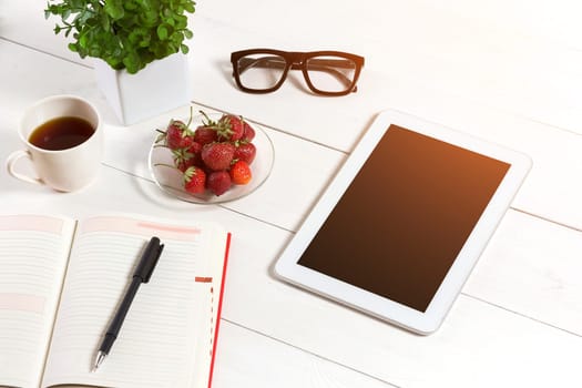 Office table desk with set of supplies, white blank notepad, cup, pen, tablet, glasses, flower on white background. Top view and copy space for text. sun flare