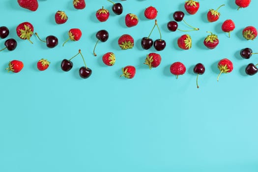 Fresh cherries and strawberries on mint background, top view. Copy space. Still life mockup flat lay