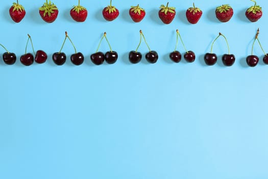 Fresh cherries and strawberries on blue background, top view. Copy space. Flat lay